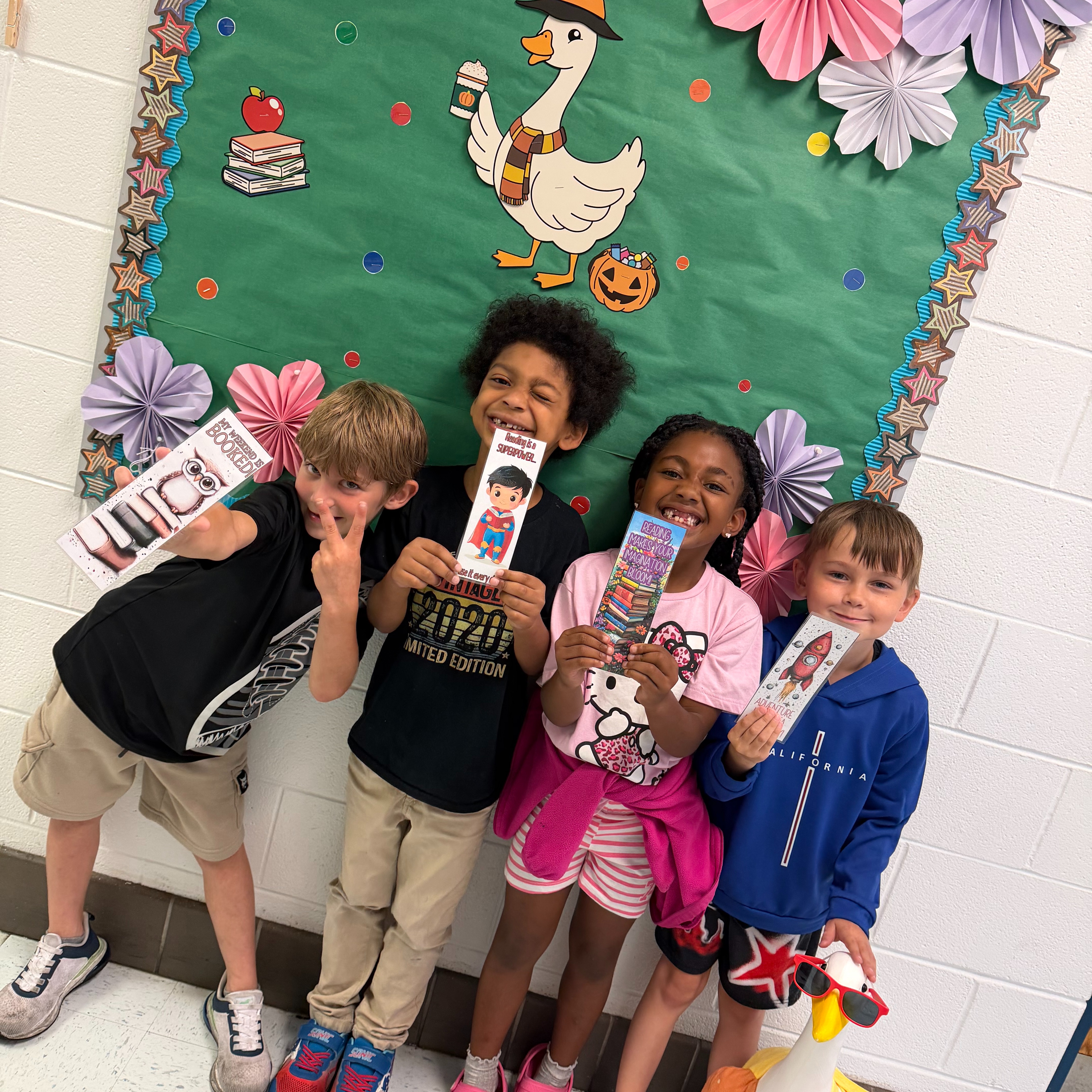 Five children stand next to each other in front of a bulletin board with Halloween decorations.