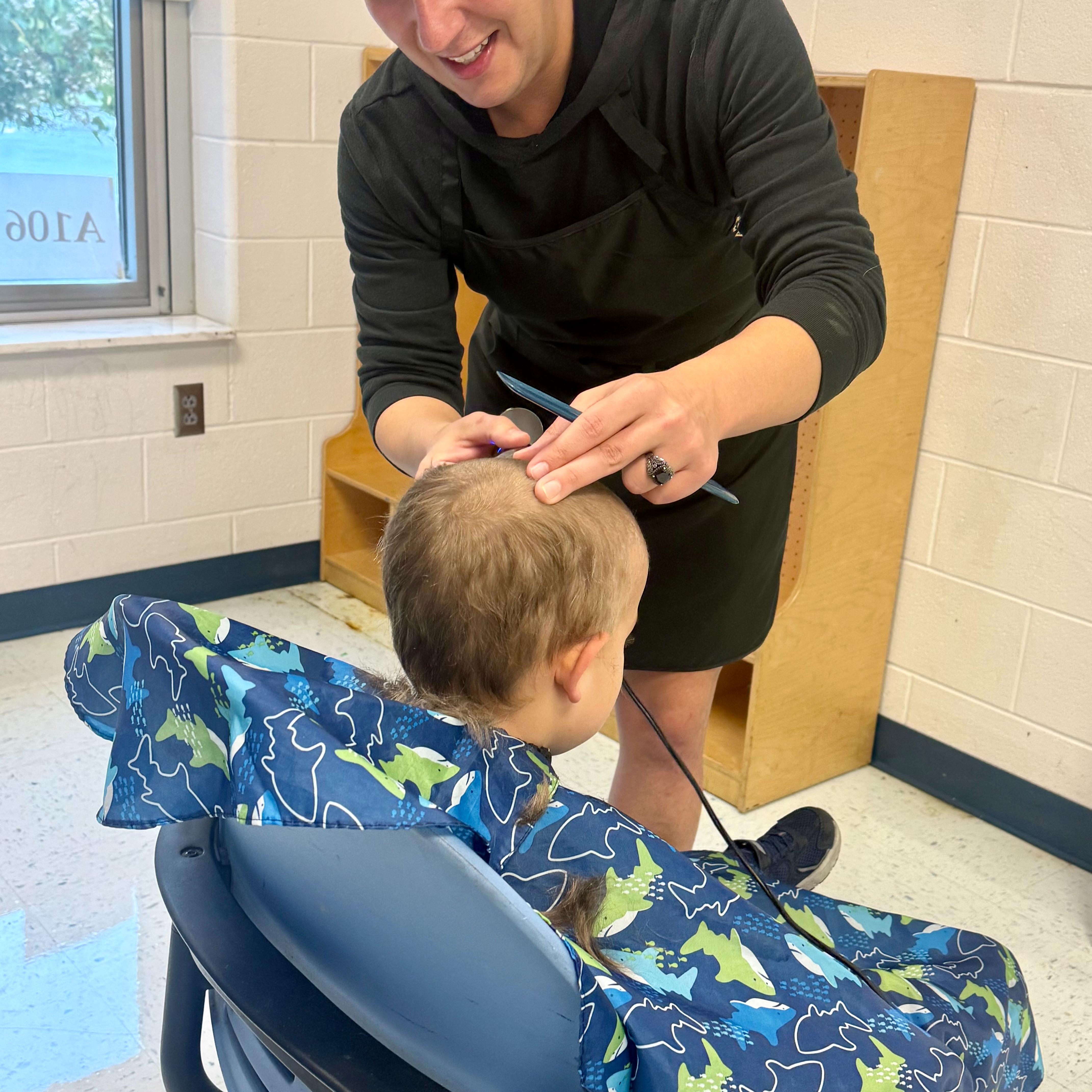 A young boy seated in a chair gets a haircut by a student volunteer.