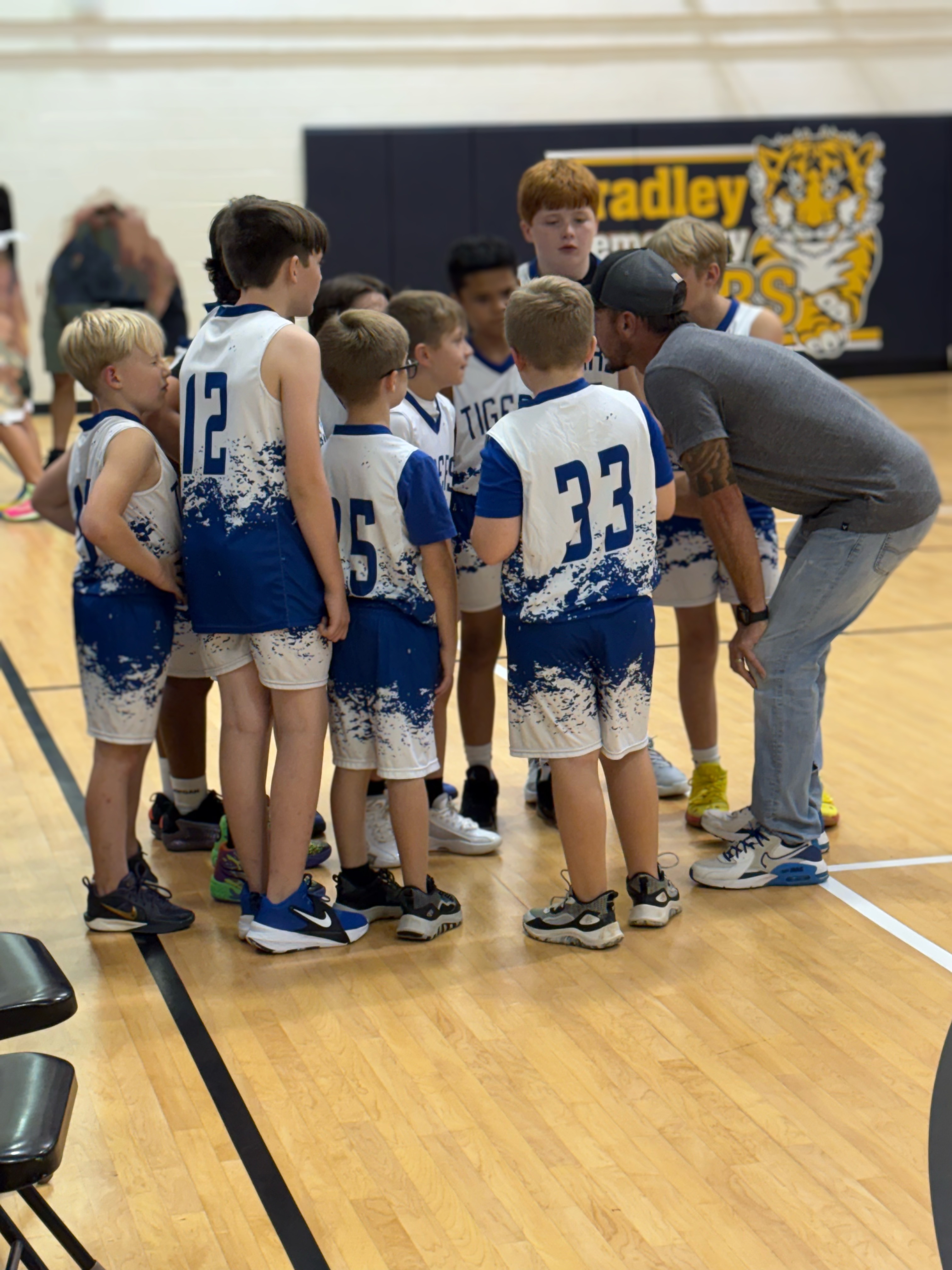 Picture of the 2025-2026 Boys Basketball Team huddling with Coach Spangler. 