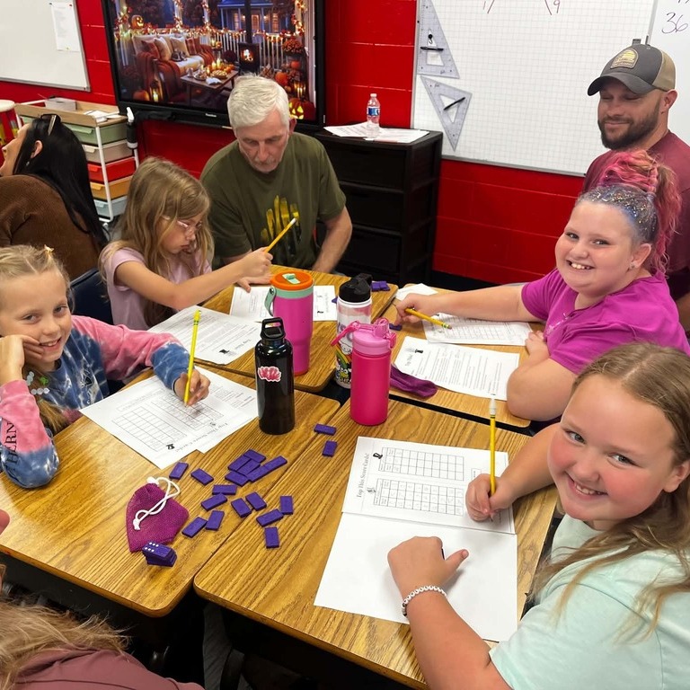 Students seated at desks in a classroom, working on paper with pencils and writing utensils.