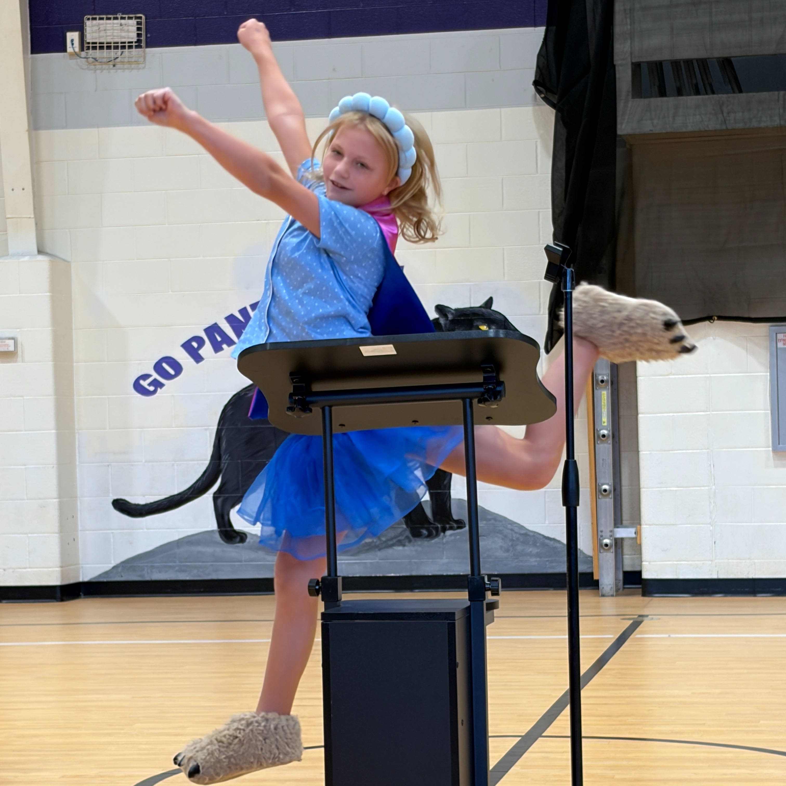 Girl dressed in blue, standing on a podium, raised her arms, and looking at the audience.