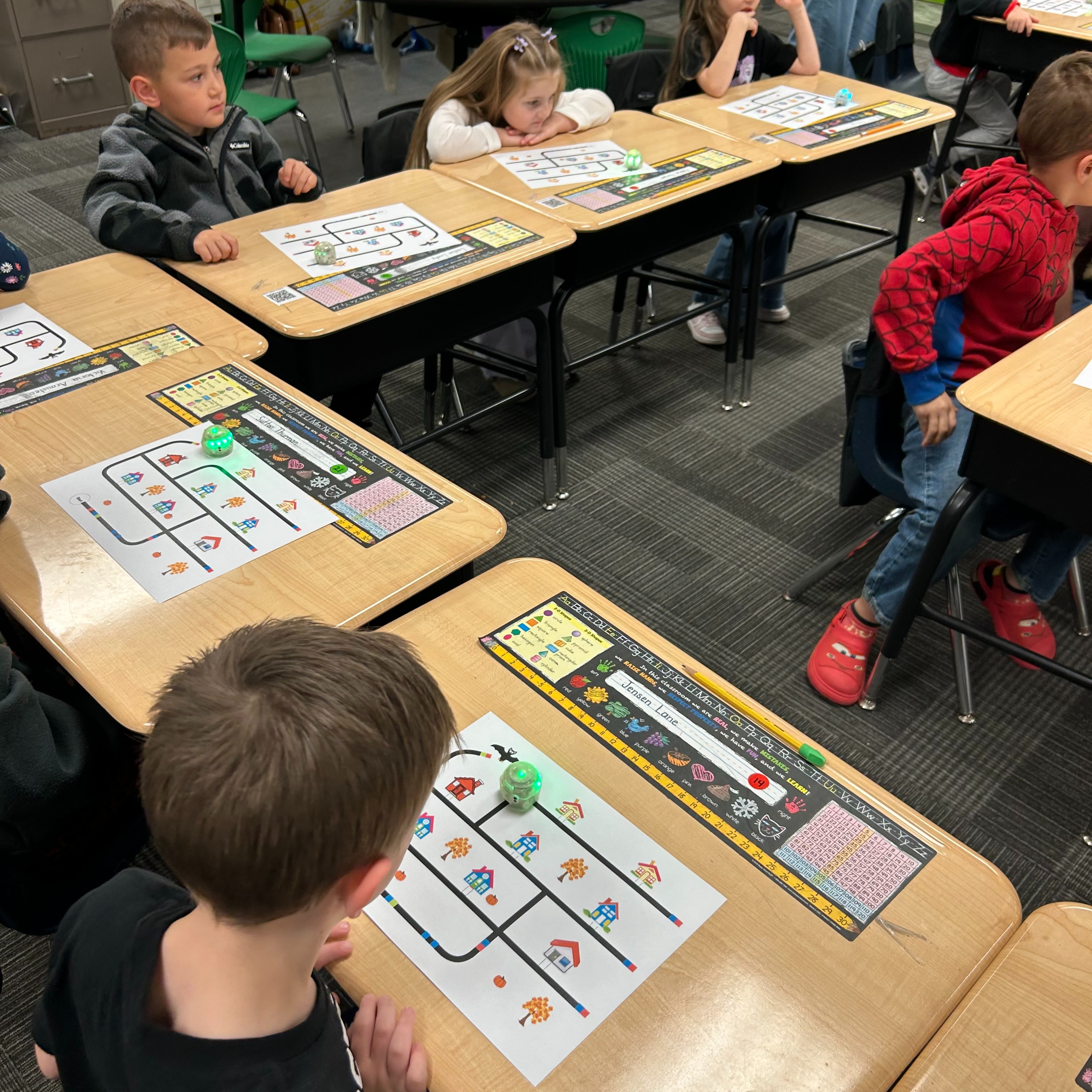 A classroom with children sitting at desks. Each child has a paper with various shapes on it.