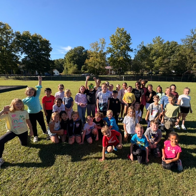 A group of children and adults posing for a photo on a field with trees.