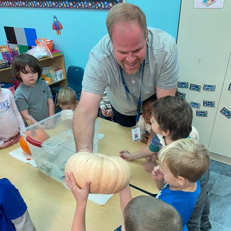 A man showing a pumpkin to a group of children who are reaching for it.