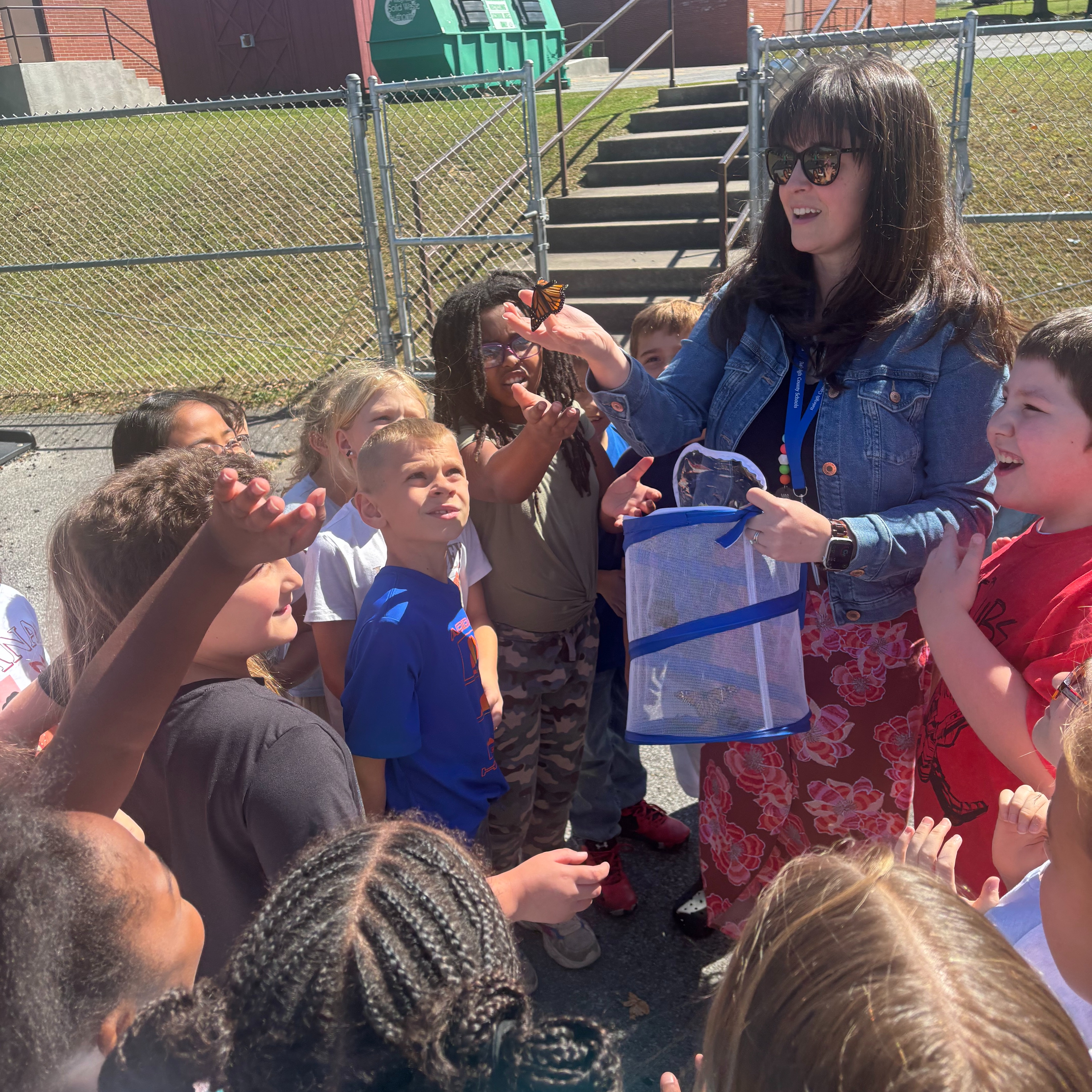 Woman with a transparent bag showing insects to a group of students outdoors.