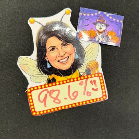 A pin features a woman with a bee costume and sign that says 98.6%. Another pin shows a dog.