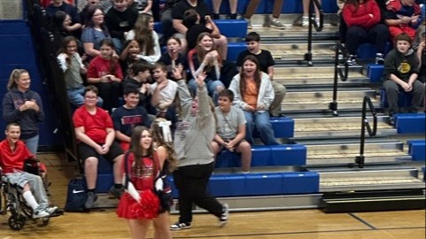 Two people playing a game with a ball while others clap; bleachers filled with spectators.