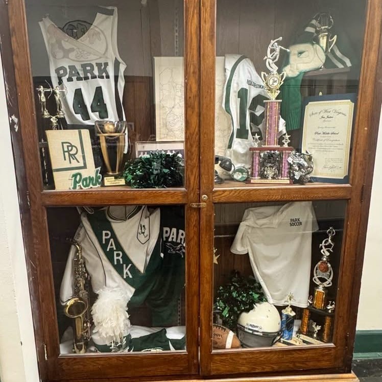 A glass-front display case with multiple items, including sports jerseys, trophies, a saxophone, and a helmet.