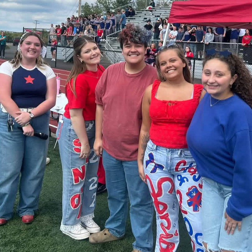 Five people in casual clothes pose for a photo in front of a red tent on a field.