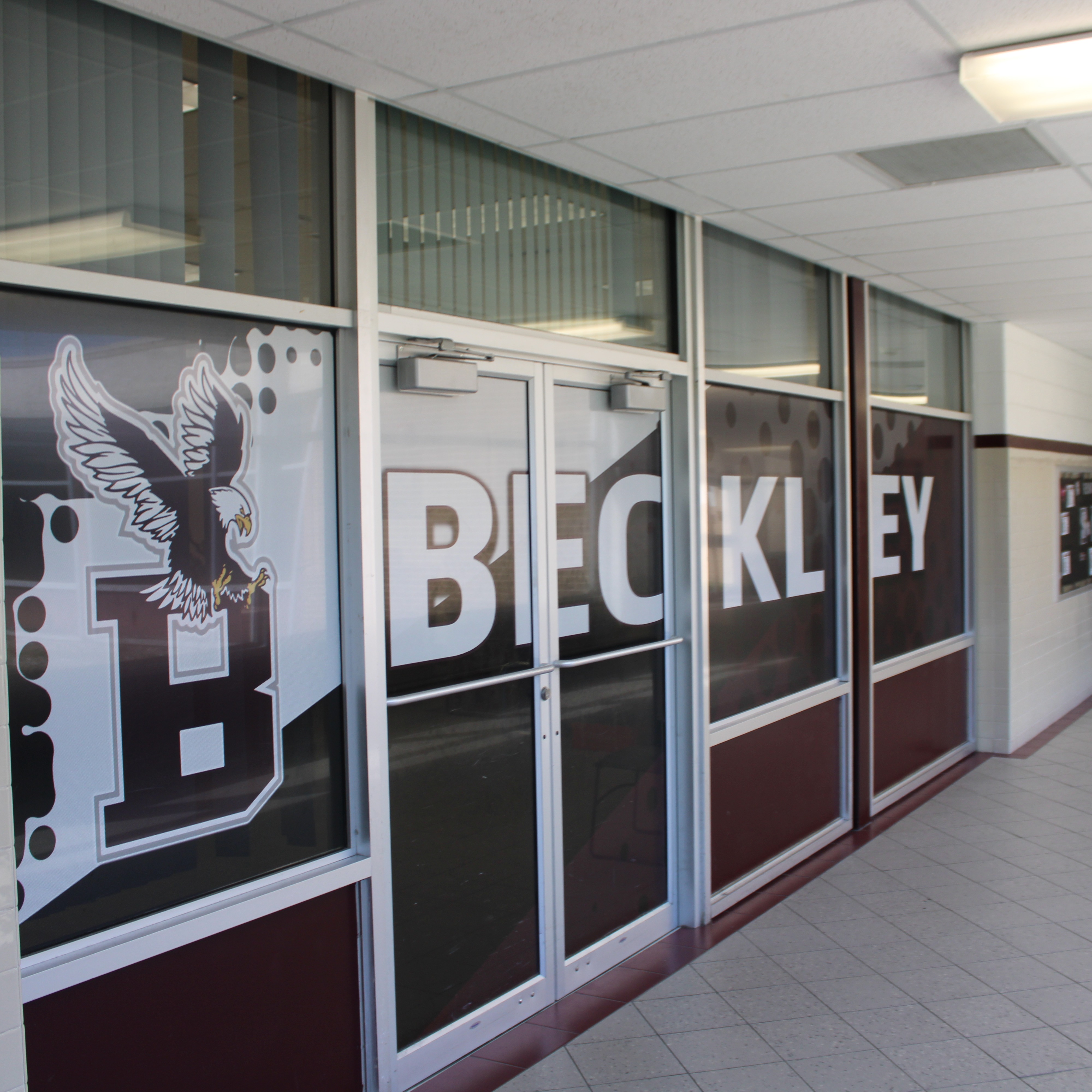 Interior hallway with white walls, tiled floor, and windows labeled with "B" and "BECKLEY". An open door leads to a hallway with fluorescent lights.